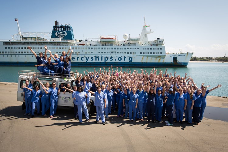 Medarbejdere på Mercy Ships står på havnemolen med hænderne i vejret